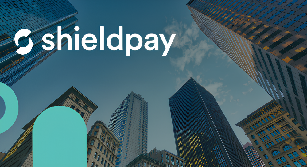 Upward view of skyscrapers under a blue sky with clouds, with the Shieldpay logo and text overlay in white and teal.