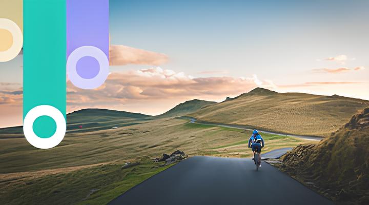 A cyclist wearing blue rides uphill on a winding road through grassy hills under a partly cloudy sky at sunset.