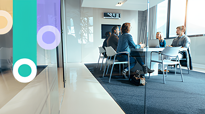 Four professionals sitting around a conference table in a modern office with large windows, engaged in a meeting.
