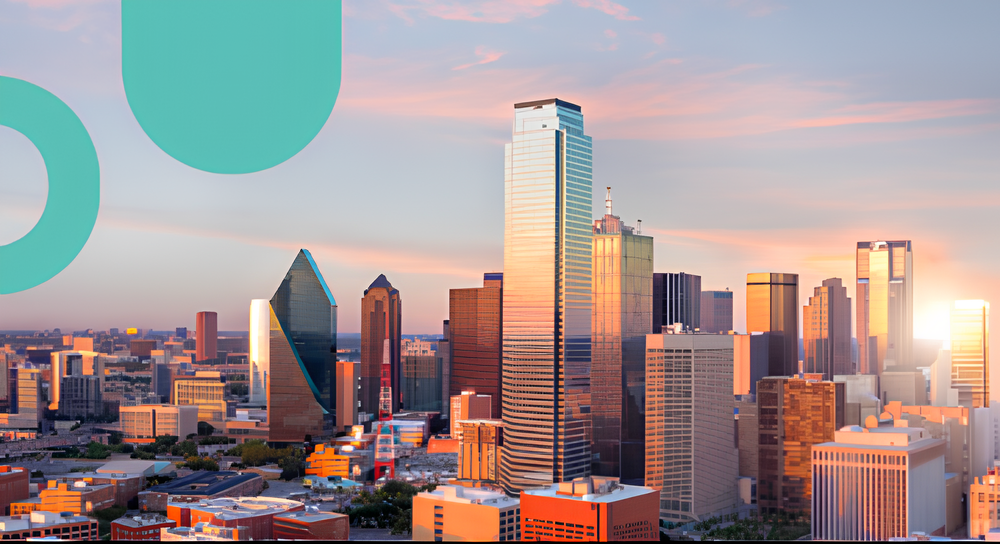 Downtown city skyline at sunset with tall modern skyscrapers reflecting the warm light and a soft pink and blue sky.
