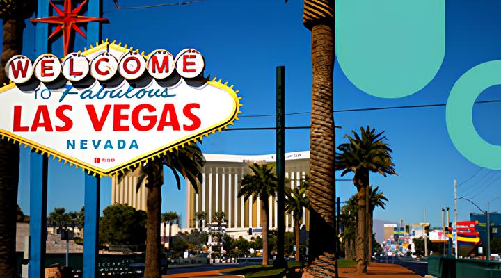 The iconic Welcome to Fabulous Las Vegas Nevada sign with palm trees and buildings under a clear blue sky in the background.