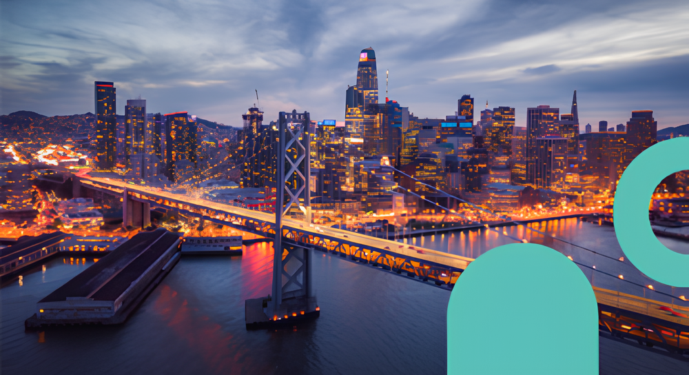View of San Francisco skyline at dusk with illuminated buildings and Bay Bridge crossing over calm water.