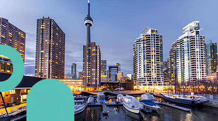 Toronto waterfront at dusk with boats docked in the marina and city skyline featuring the illuminated CN Tower and high-rise buildings in the background.