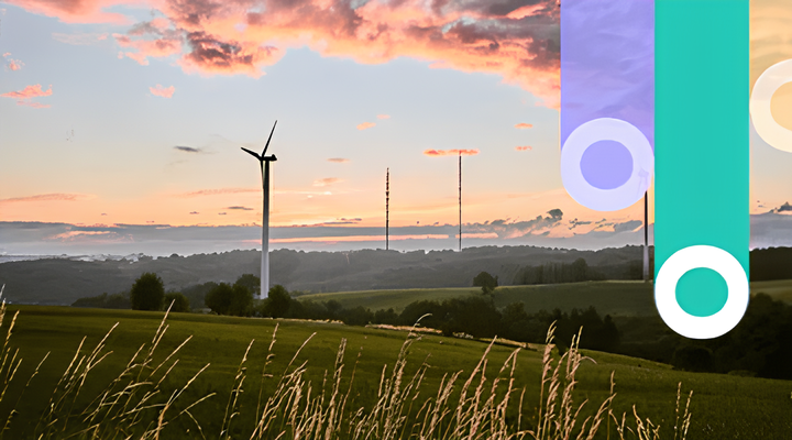 A wind turbine stands in a grassy field with rolling hills in the background under a colorful sunset sky with scattered clouds.
