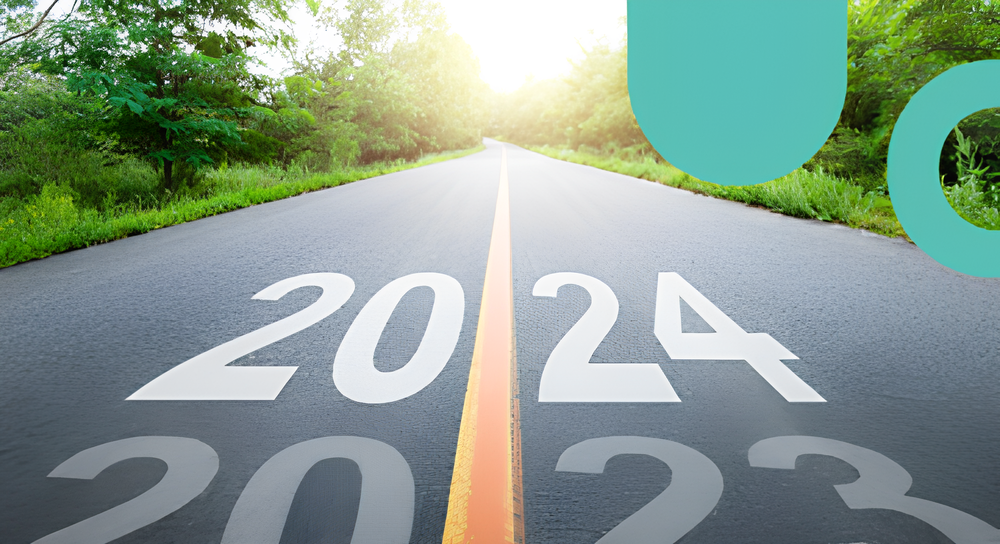 A paved road surrounded by green trees with the numbers 2023 fading away and 2024 prominently painted on the road, symbolizing moving forward into the new year.