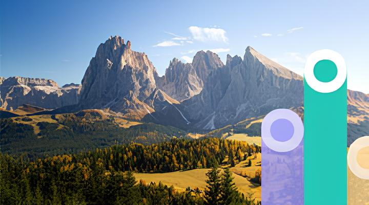 Sunlit mountain range with rocky peaks above a forest and grassy valley under a clear blue sky.