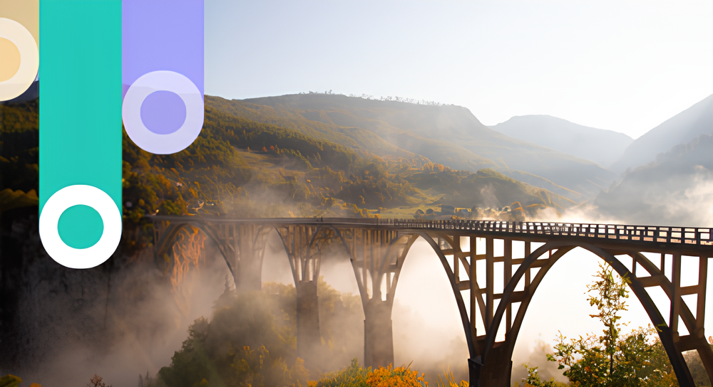 A long arched bridge spanning a foggy valley with hills and mountains in the background under a clear sky during sunrise or sunset.