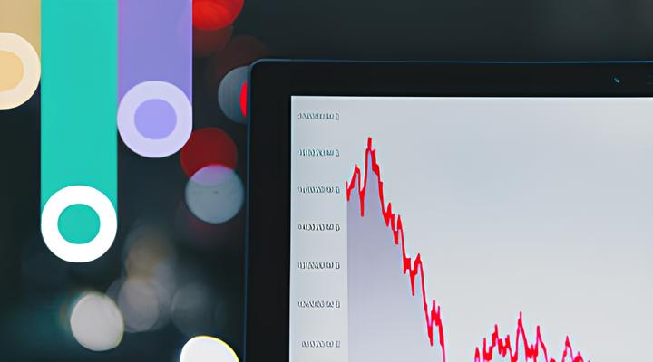 Close-up of a computer screen displaying a red line graph trending downward on a white background with blurred multicolored lights in the background.