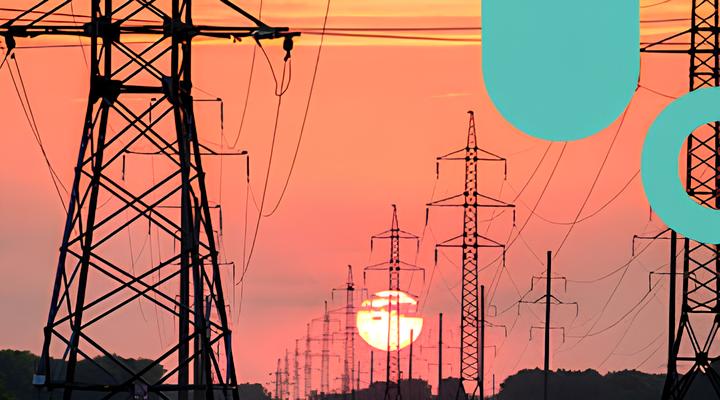 Sunset behind a series of tall electrical transmission towers with power lines stretching across an orange-pink sky.