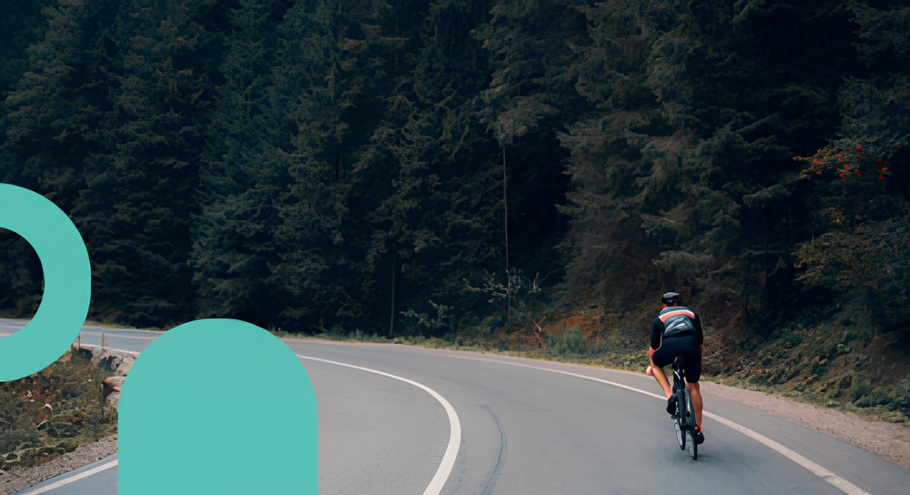 Cyclist riding on a winding road surrounded by dense forest.