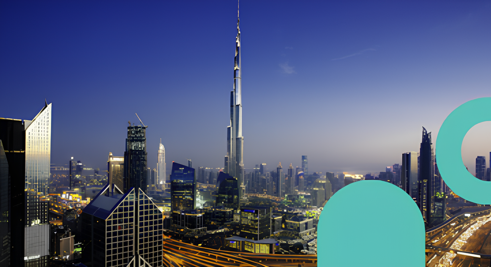Panoramic view of a modern city skyline at dusk with illuminated skyscrapers and a tall, slender tower prominently in the center under a clear blue sky.