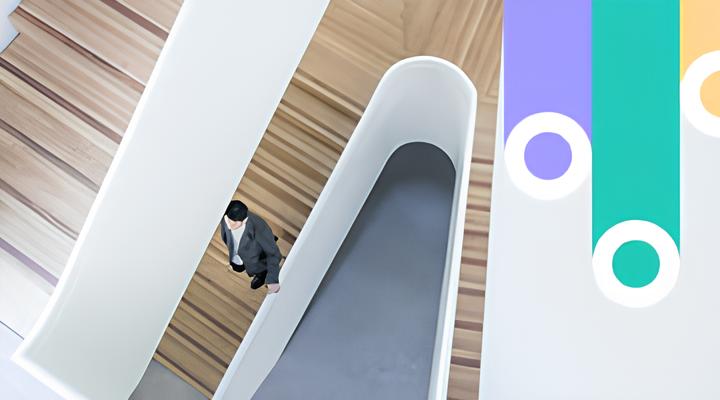 A man in a suit walking up a modern curved wooden staircase with white railings, viewed from above, with a colorful abstract design on the right side of the image.