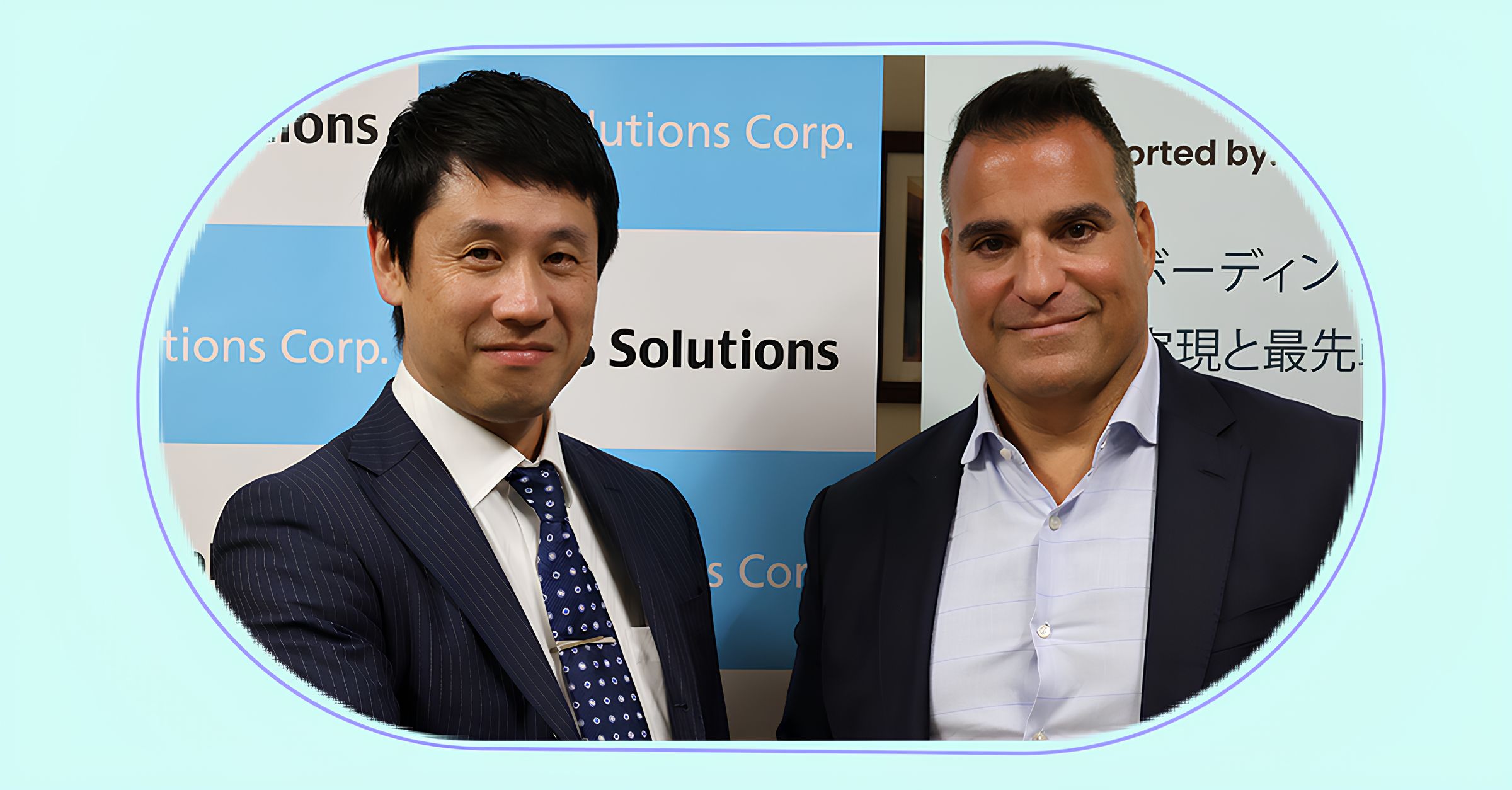 Two men in business attire standing side by side, smiling, in front of a blue and white backdrop with partial text including 'Solutions Corp.' and some Japanese characters.