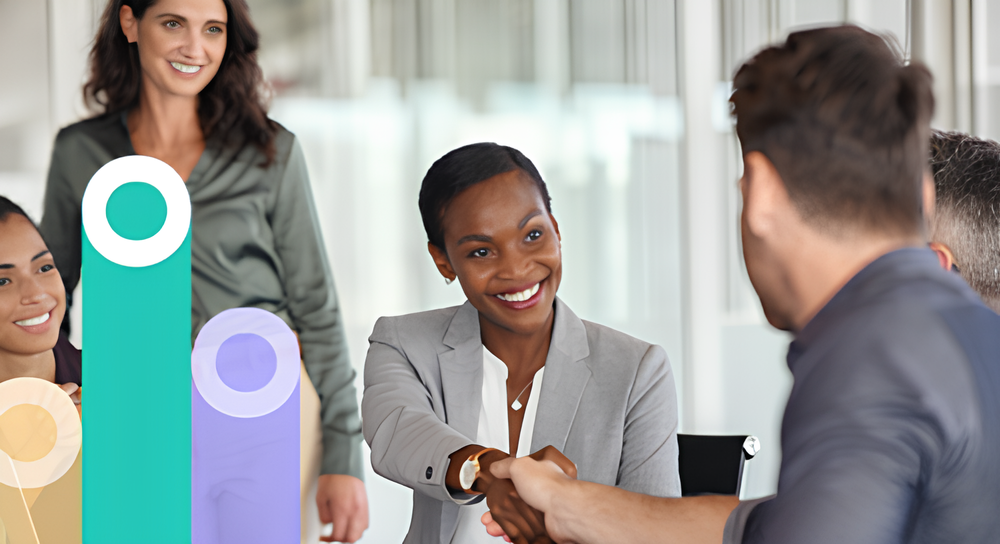 Businesswoman in a gray blazer smiling and shaking hands with a man in a corporate office, with colleagues in the background and a translucent bar graph overlay.