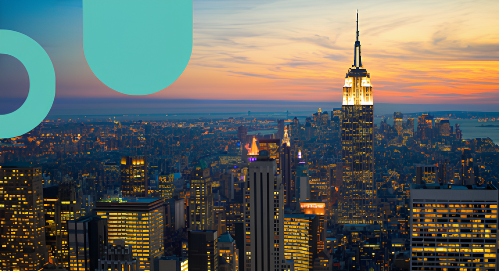 City skyline at sunset featuring the illuminated Empire State Building among other high-rise buildings with a colorful sky in the background.