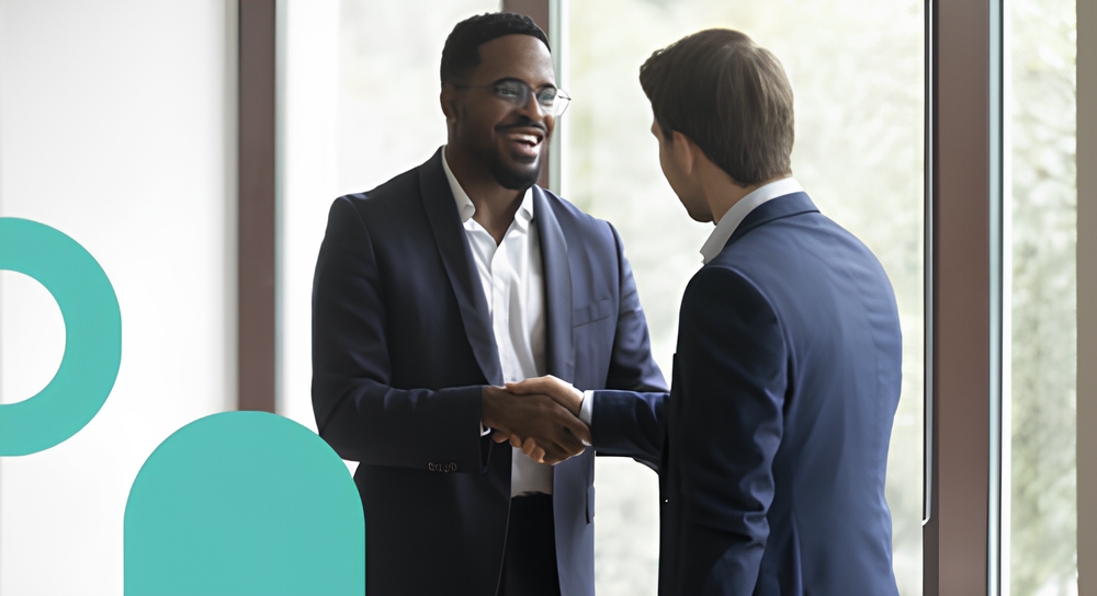 Two men in business suits shaking hands near a large window during a professional meeting.