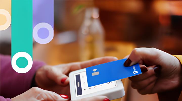 A person holding a white card reader while another person taps a blue contactless payment card on it for payment.