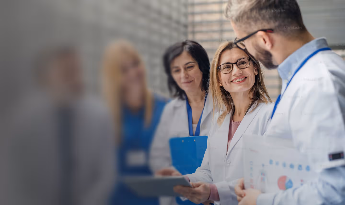 Group of medical professionals in lab coats discussing with tablets and charts, smiling and collaborating.
