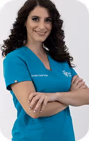Smiling woman with curly dark hair wearing teal medical scrubs with crossed arms.