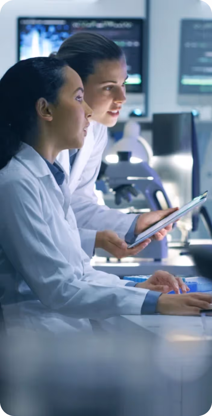 Male doctor wearing glasses and a white coat with a stethoscope around his neck, sitting at a desk with hands clasped.