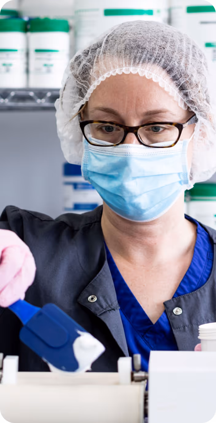 Male doctor wearing glasses and a white coat with a stethoscope around his neck, sitting at a desk with hands clasped.
