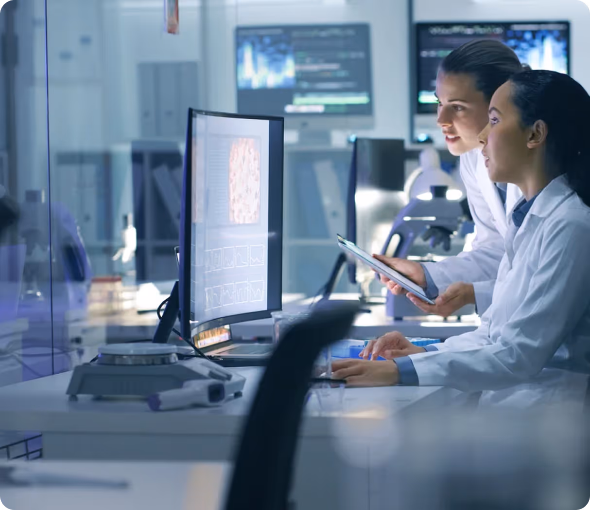 Group of medical professionals in lab coats discussing with tablets and charts, smiling and collaborating.