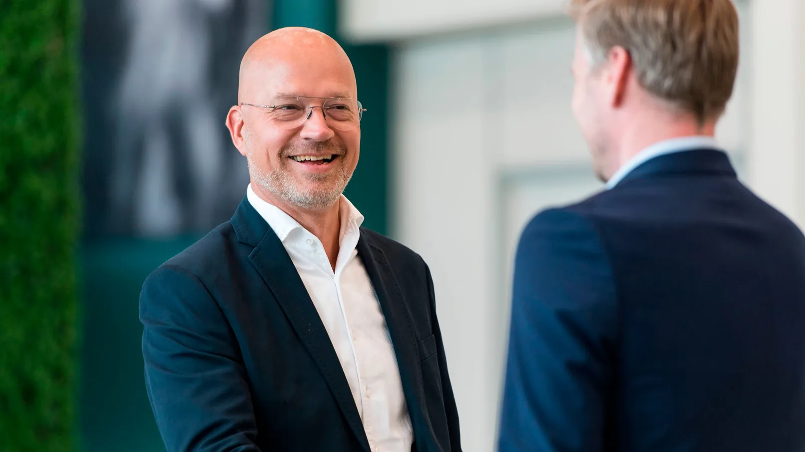 Een foto van twee mannen die kijken naar een tablet en overleggen. Op de achtergrond zijn schermen met aandelen te zien. Daarover staat het logo en een quote van Van Ameyde