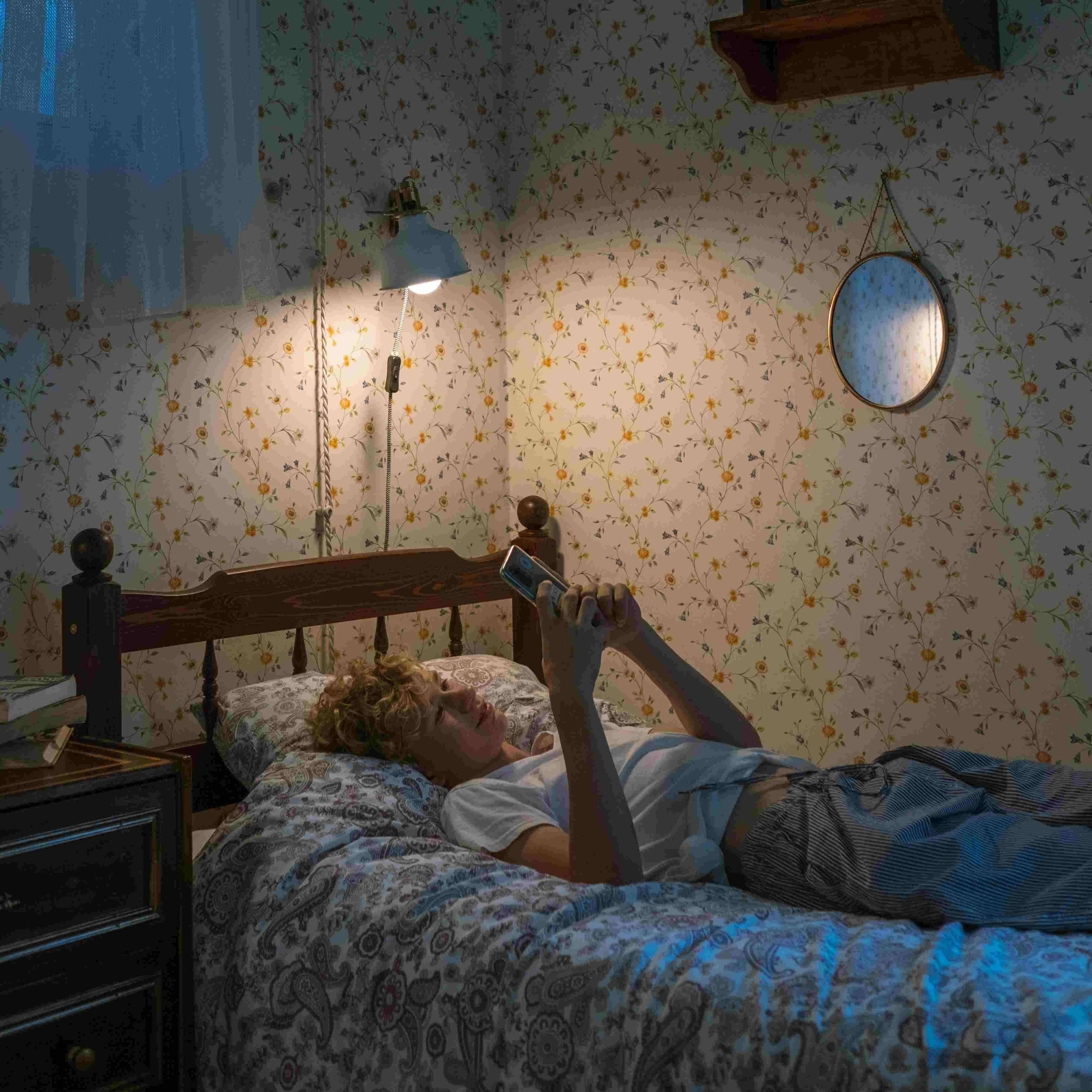 A teenager lays on their bed while on their phone.