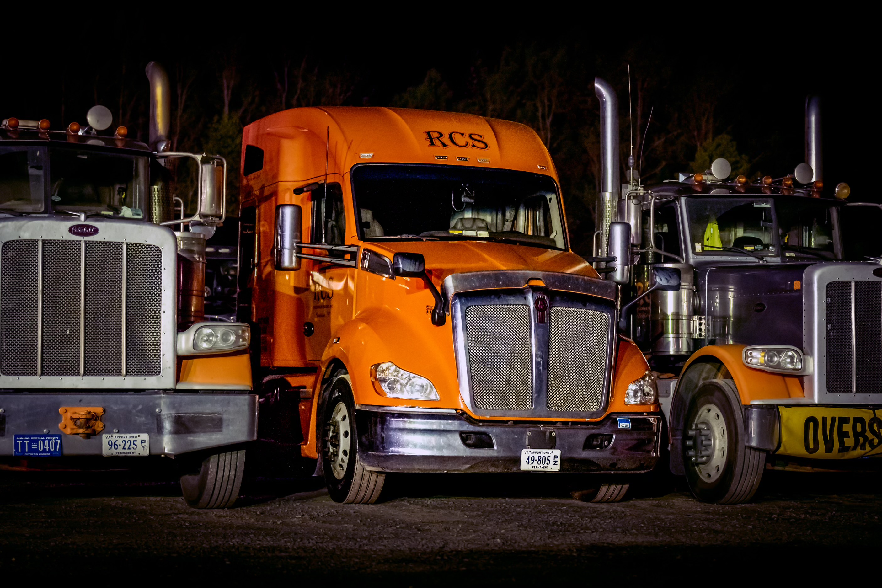 Black RCS Trucking semi-truck with chrome grille and orange logo, parked outdoors on a clear day.