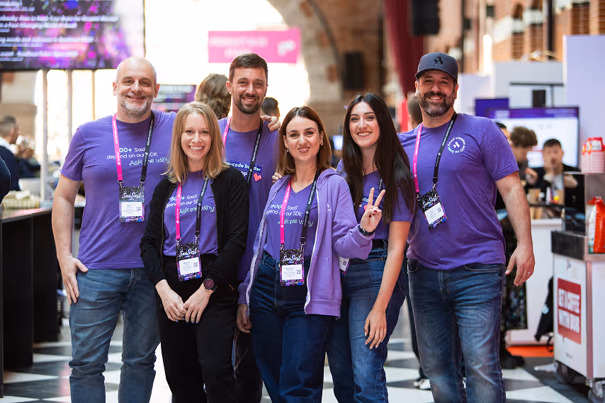 BeeFree developers team smiling at tech event booth, wearing branded purple shirts and conference badges.