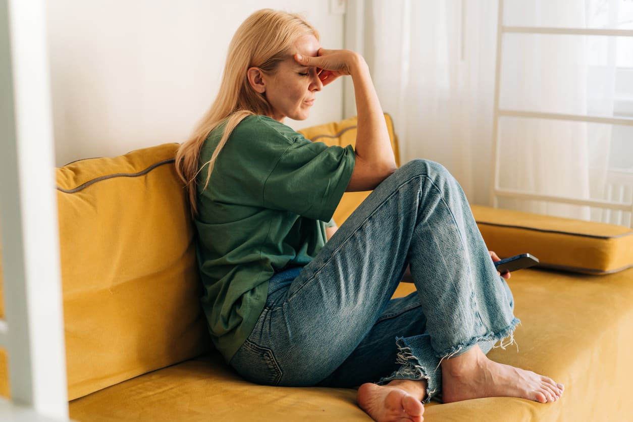 traurige Frau mittleren Alters, die zu Hause auf dem Sofa sitzt.