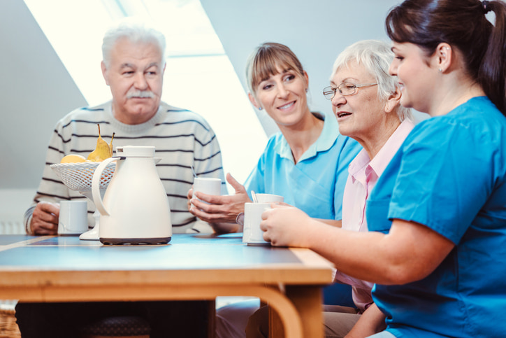 Senioren und Altenpflegehelferinnen bei Kaffeezeit im Pflegeheim
