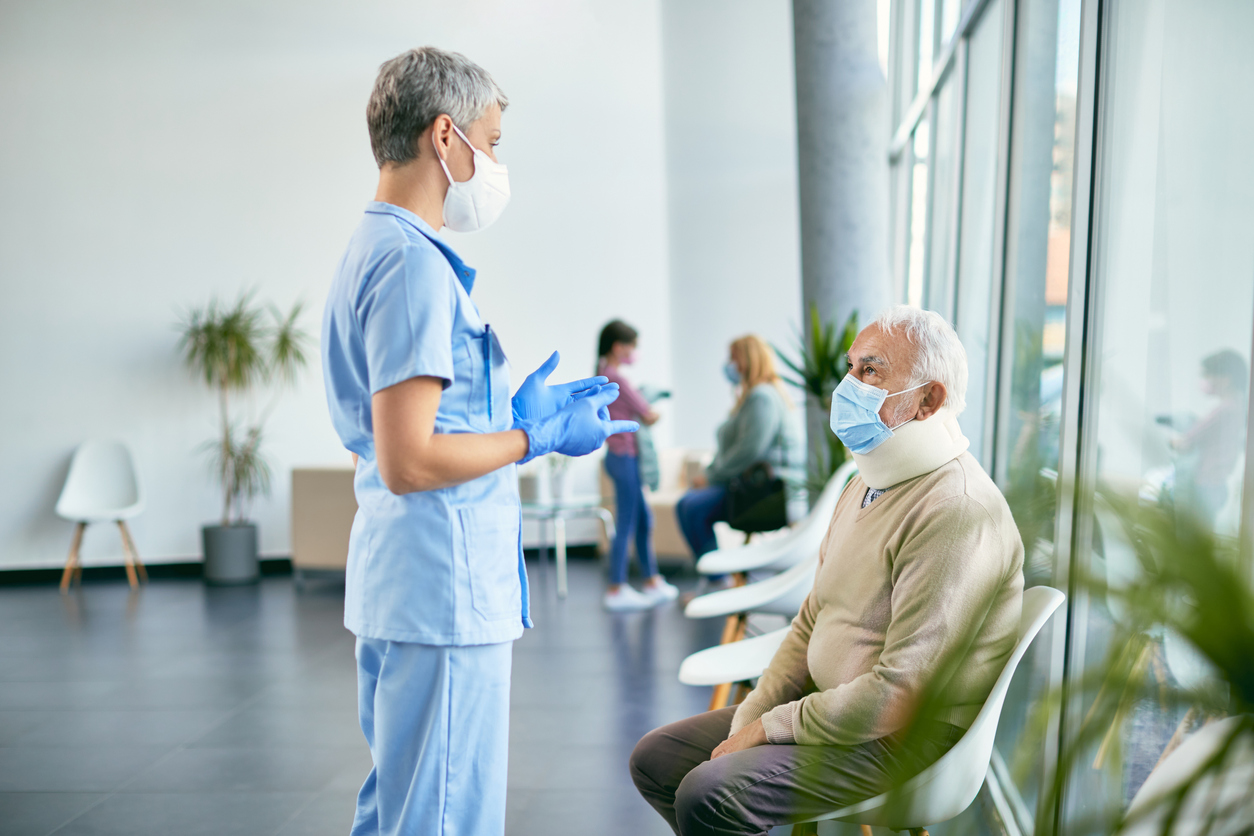 Krankenschwester kommuniziert mit Senior-Patienten, die auf die medizinische Untersuchung seines verletzten Halses in der Klinik wartet.