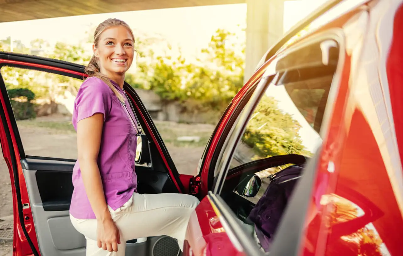 Lächelnde kaukasische junge erwachsene Gesundheitsarbeiterin, die nach einem sehr anstrengenden Arbeitstag in ihr Auto steigt