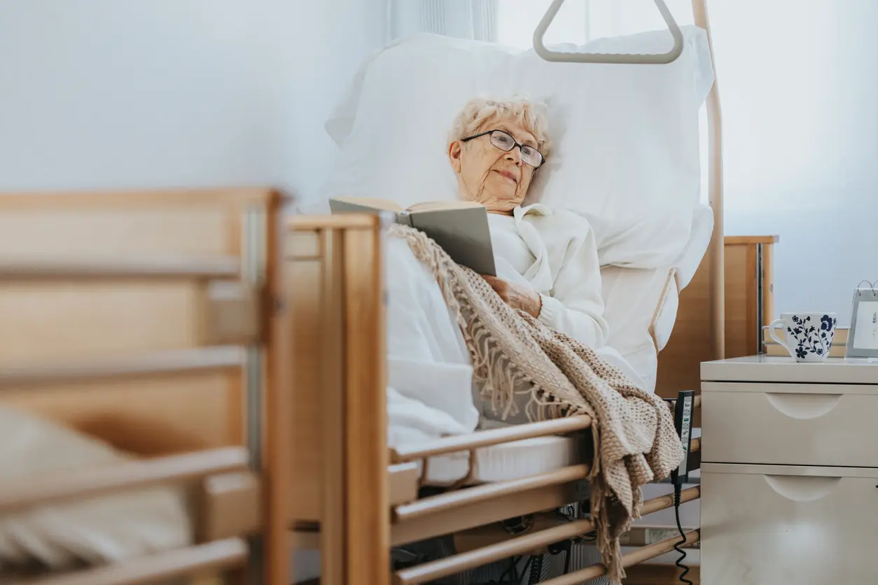ranke Seniorin liegt in einem Krankenhausbett mit Gittern und liest ein Buch