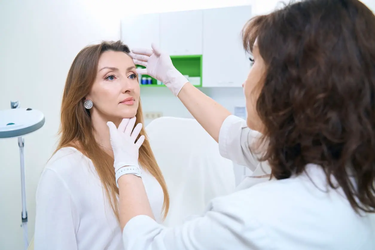 Patient sitzt auf einem Stuhl bei der Untersuchung durch einen Dermatologen