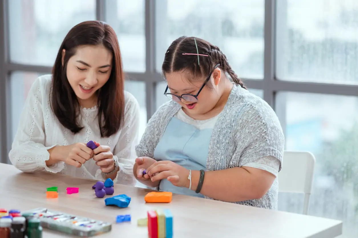 Mädchen mit Downsyndrom baut mit Heilerziehungspflegerin mit Klötzen