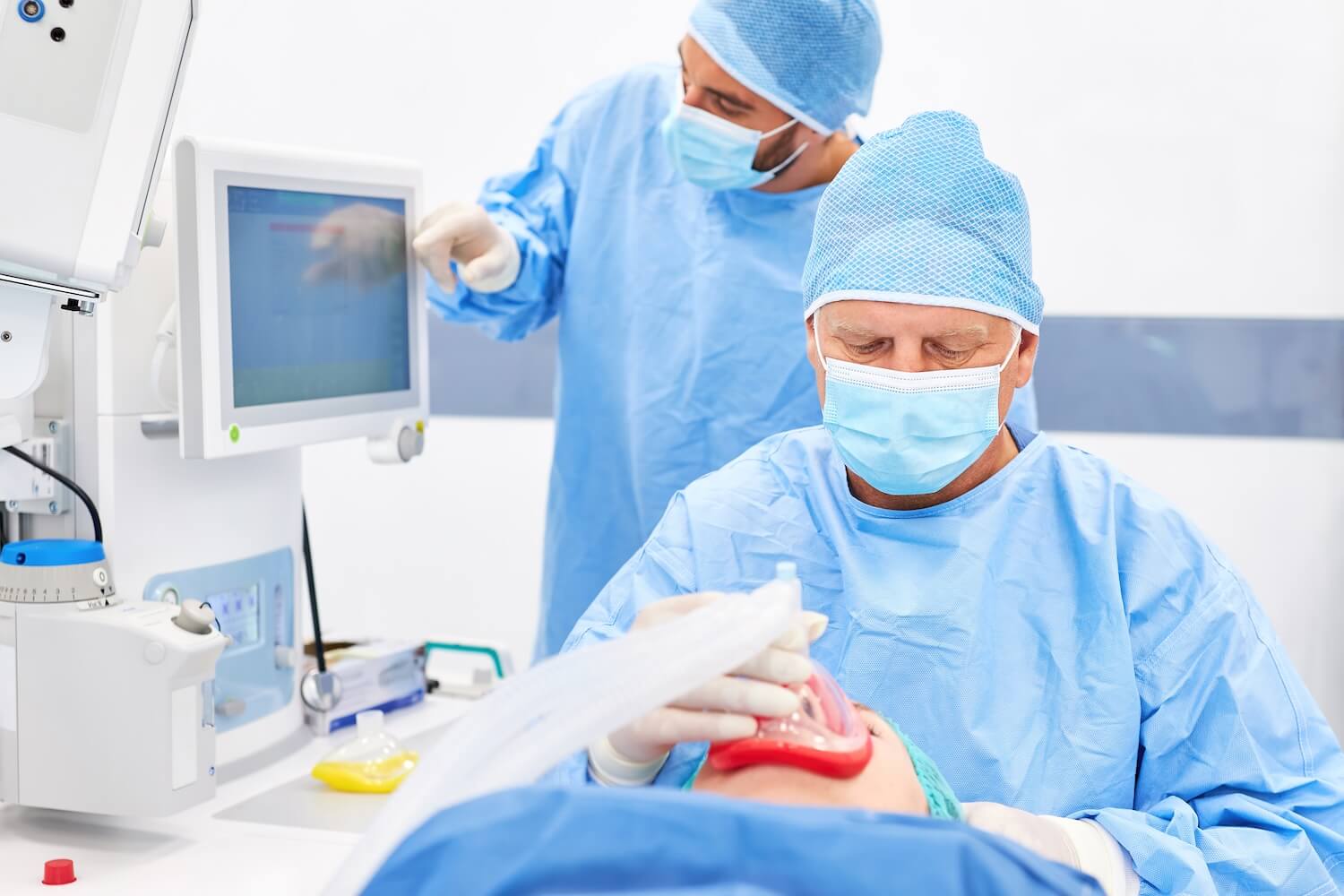 Zwei Anästhesisten oder ATAs überwachen während eines Eingriffs die Narkose an einem modernen Überwachungsgerät, während ein Patient beatmet wird.