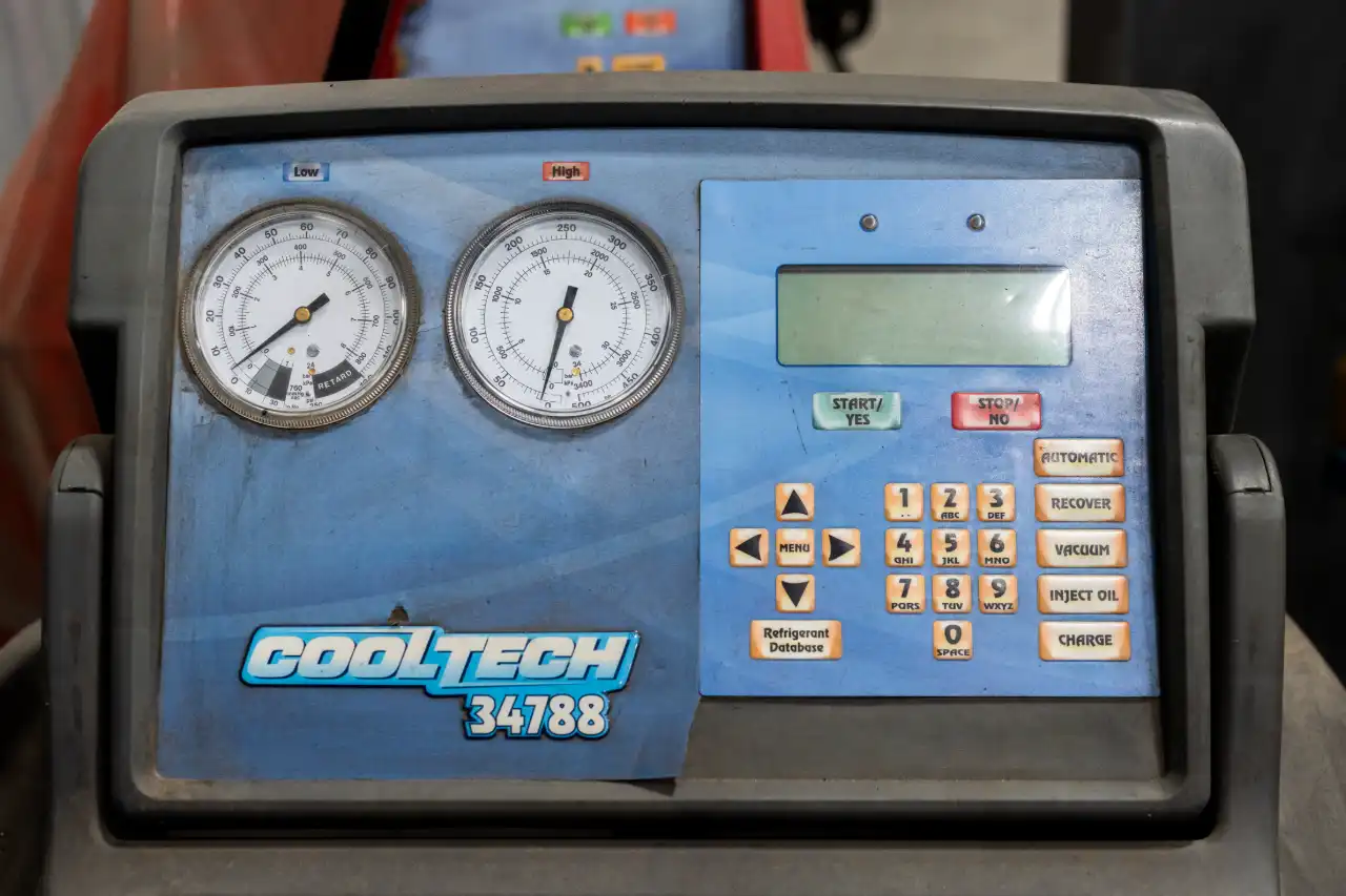A/C refrigerant recovery tool displays low-high gauges, keypad and “COOLTECH 34788” label inside fleet service bay.