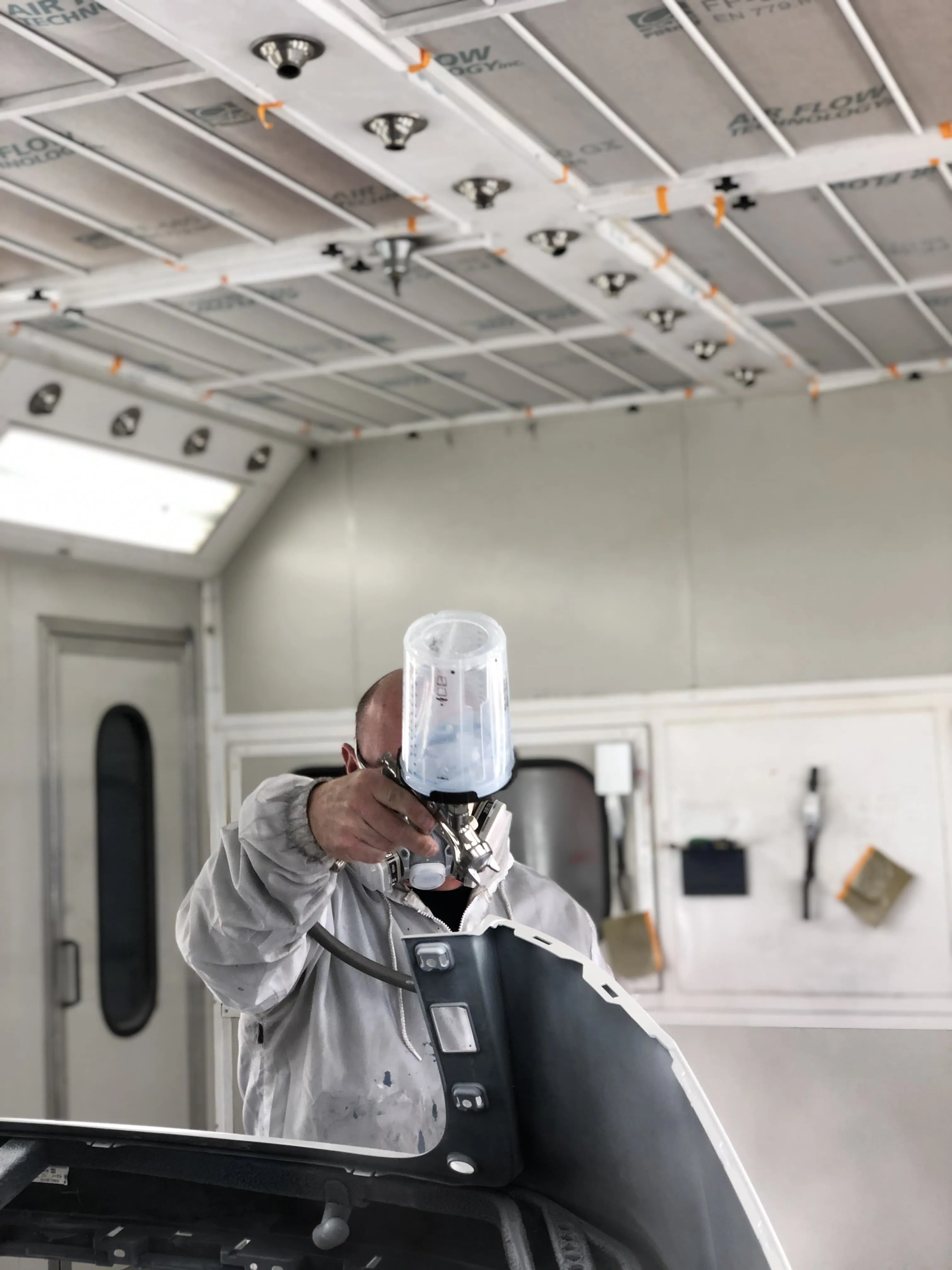 A car painter painting a front bumper in a paint booth in Omaha, NE