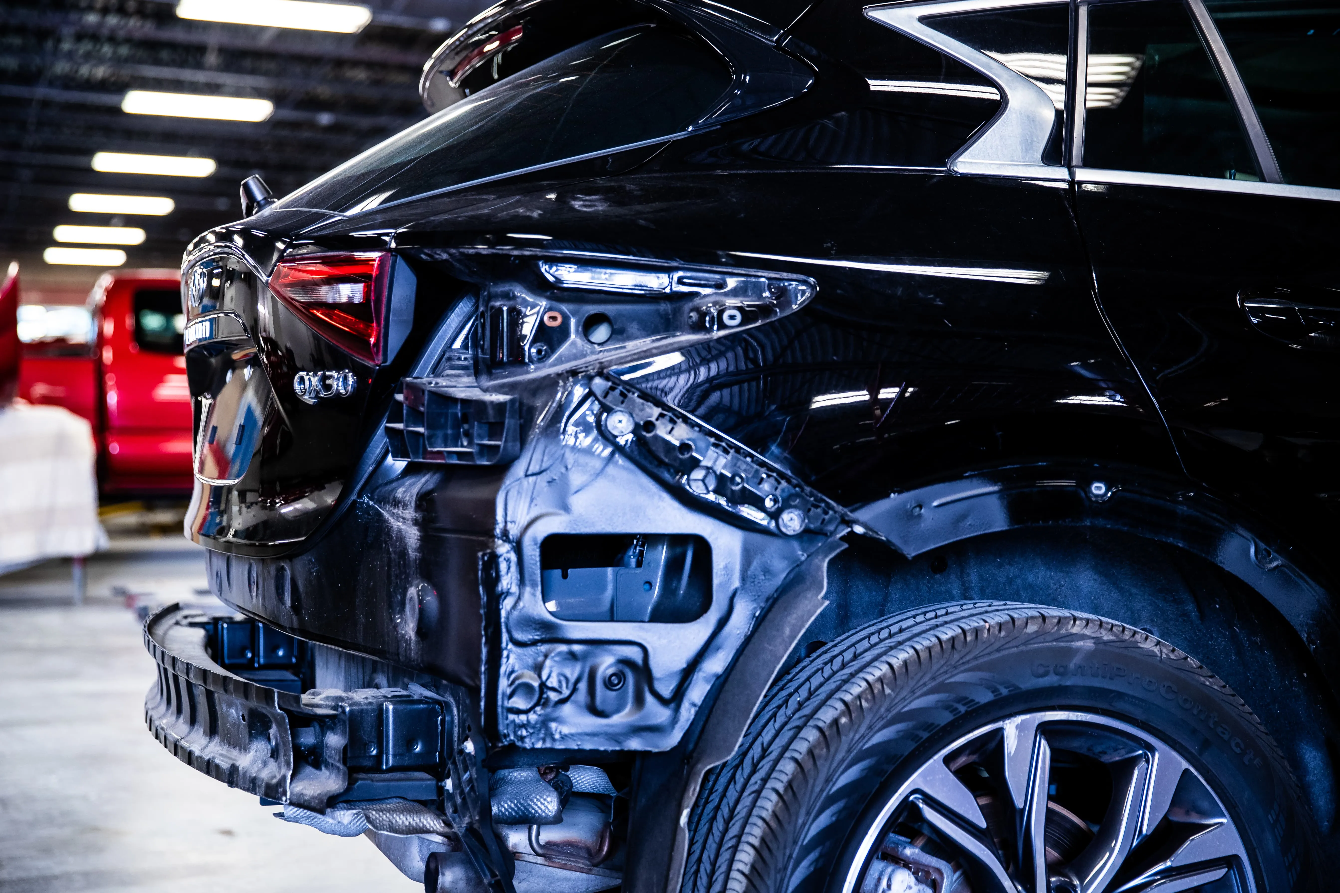 Rear side of a black car with visible damage and missing parts inside a garage or workshop.