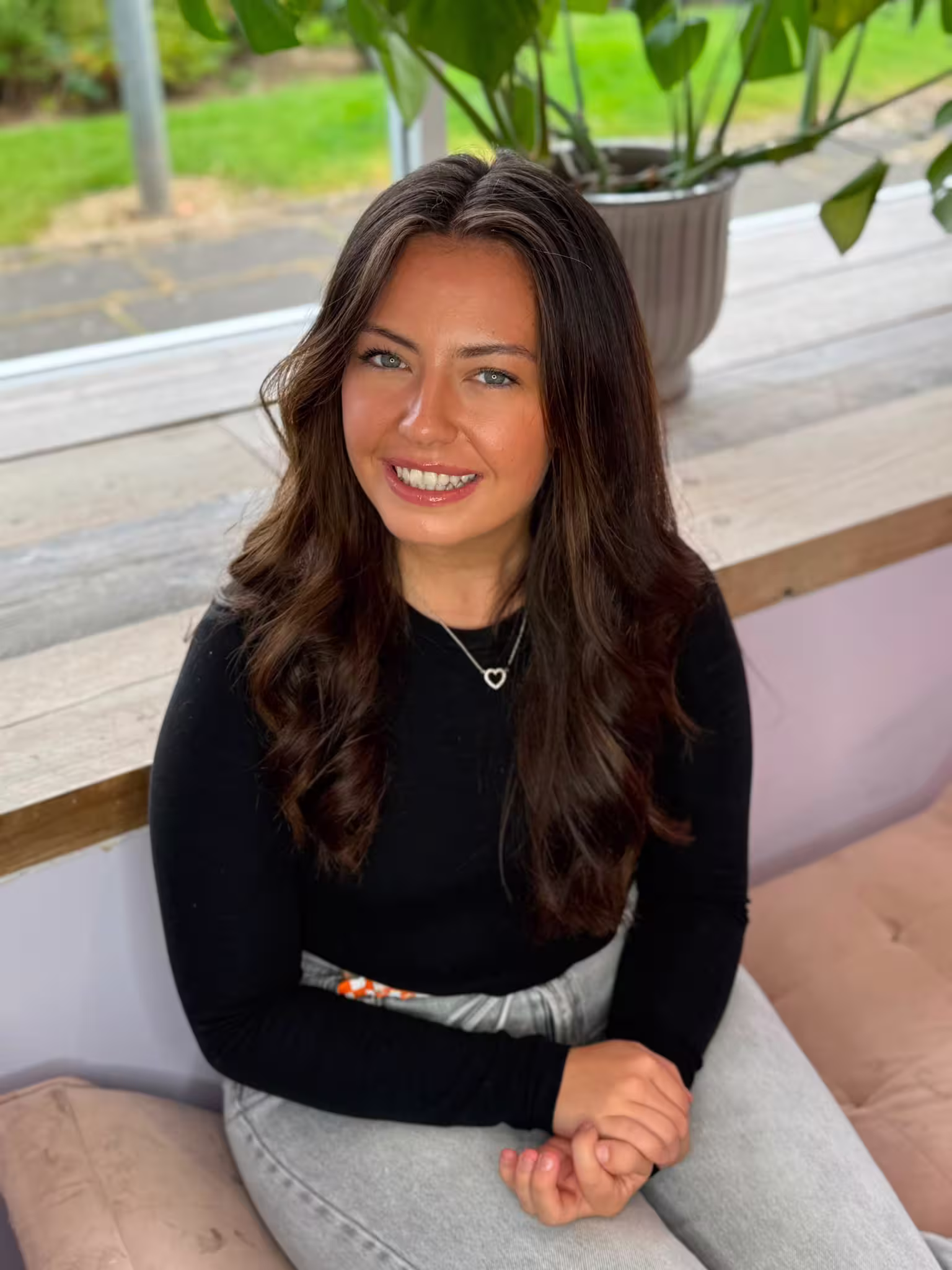 Abbie has long dark hair, smiling brightly at camera, wearing a black top and blue jeans