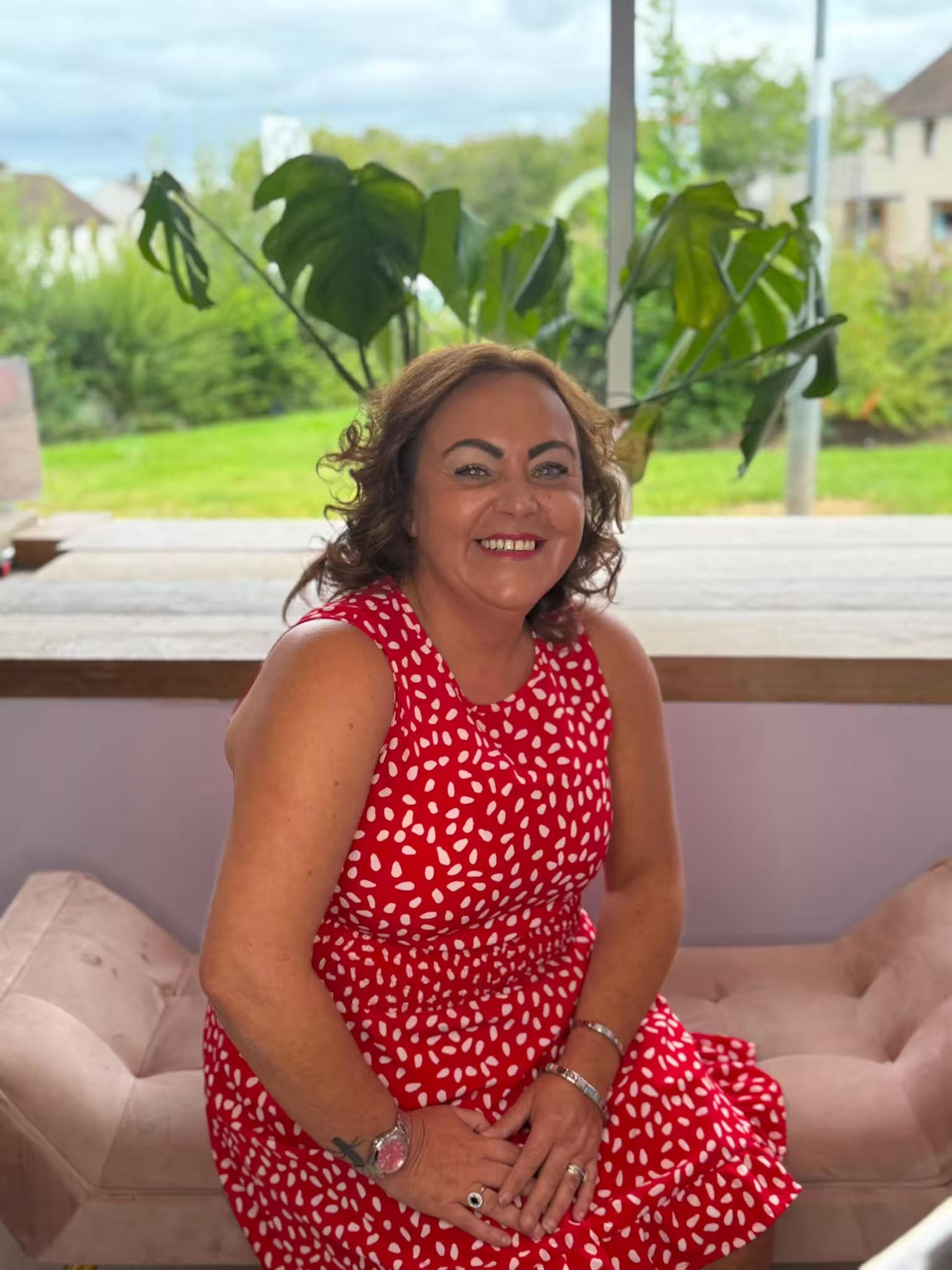 Amanda has short, curly dark brown hair, beaming a wide smile at the camera, wearing a red and white spotted dress