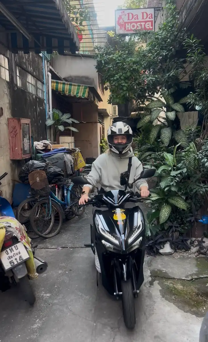 Rider in a full face helmet on a rented automatic scooter in a Chiang Mai alley