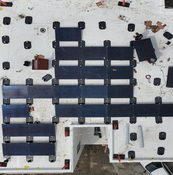 An overhead drone shot captures the installation of solar panels on a bright, flat commercial rooftop