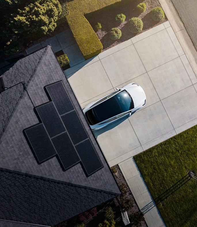 Aerial view of Tesla solar panels installed on a home roof beside a driveway with a parked car
