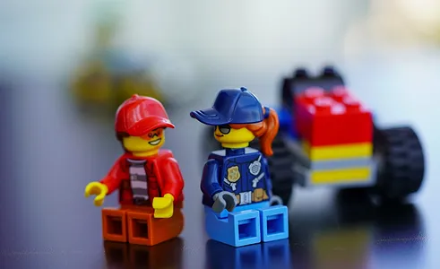 Two Lego minifigures sitting on a reflective surface, one dressed as a police officer and the other wearing a red cap.