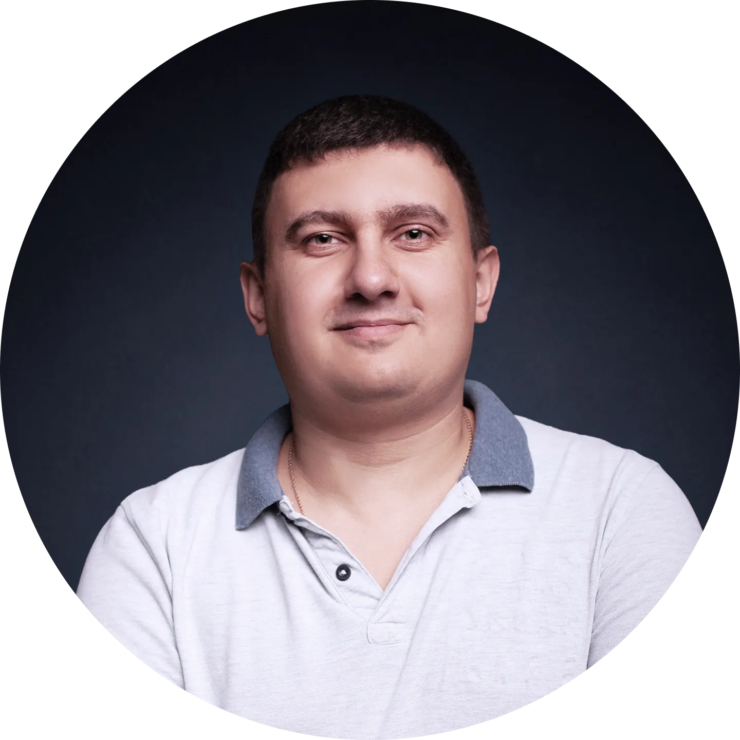 Portrait of a man with short dark hair wearing a white polo shirt with a grey collar, against a dark background.