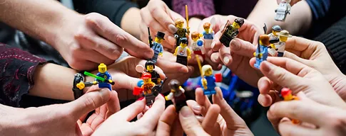 Multiple hands holding and pointing small colorful toy figurines together in a circle.