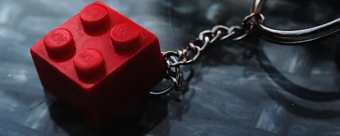 Close-up of a red LEGO brick keychain on a dark textured surface.